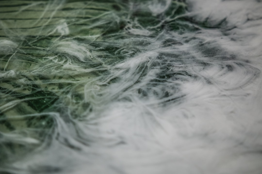 This experimental painting features green and black swirls beneath a few layers of clear and white epoxy resin. The technique I use to create this kind of paint texture is called “fluid art,” and it relies on mixing a variety of mediums into acrylic paints to influence how they interact. I’ll use materials like glue, isopropyl alcohol, liquid silicone, and a butane torch.